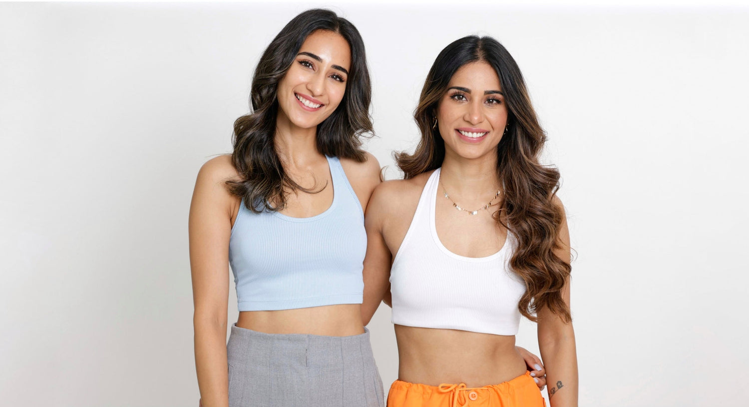 Two women smiling, standing side by side, wearing crop tops.
