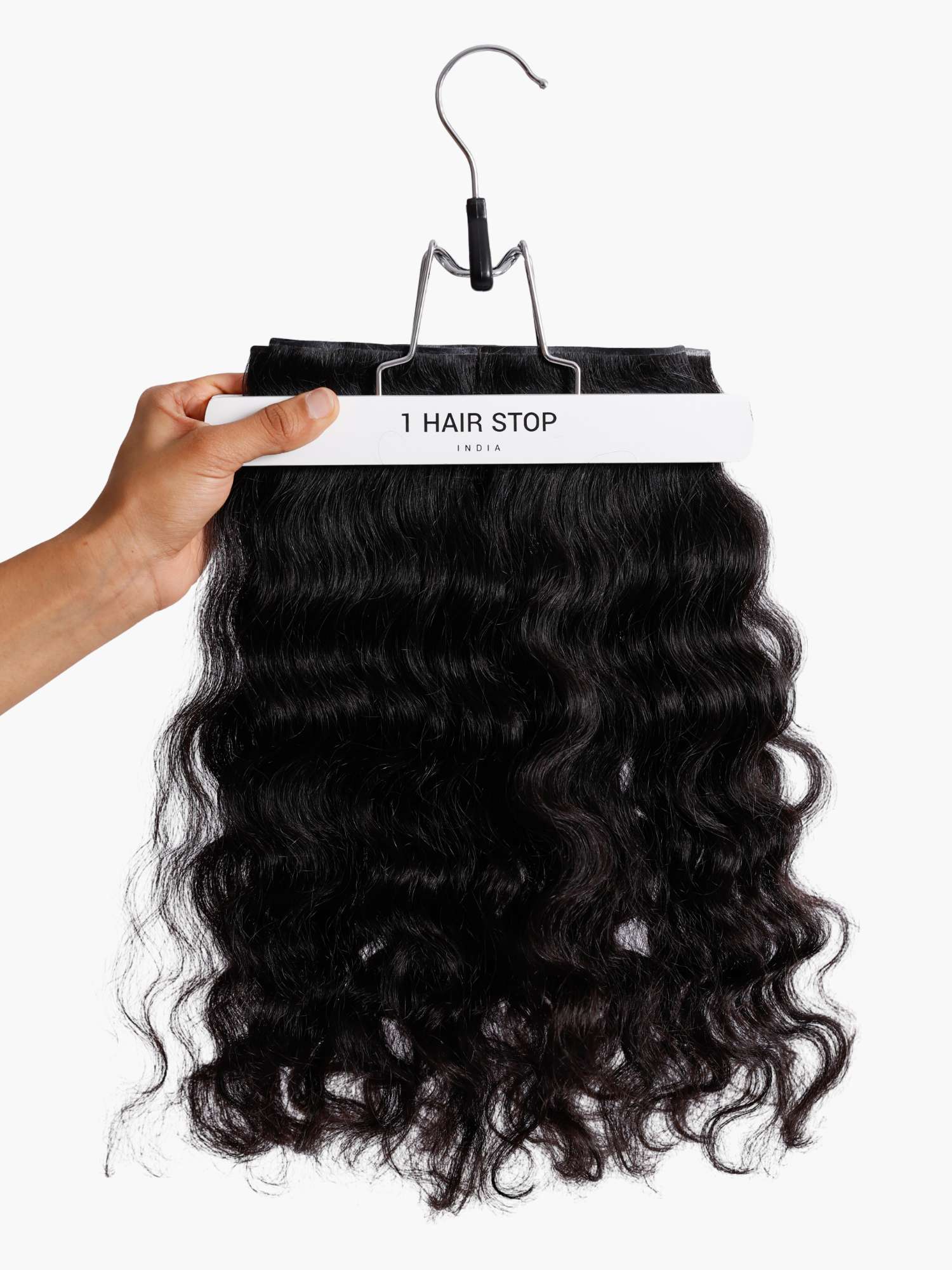 A hand holding a set of curly clip-in hair extensions on a hanger.