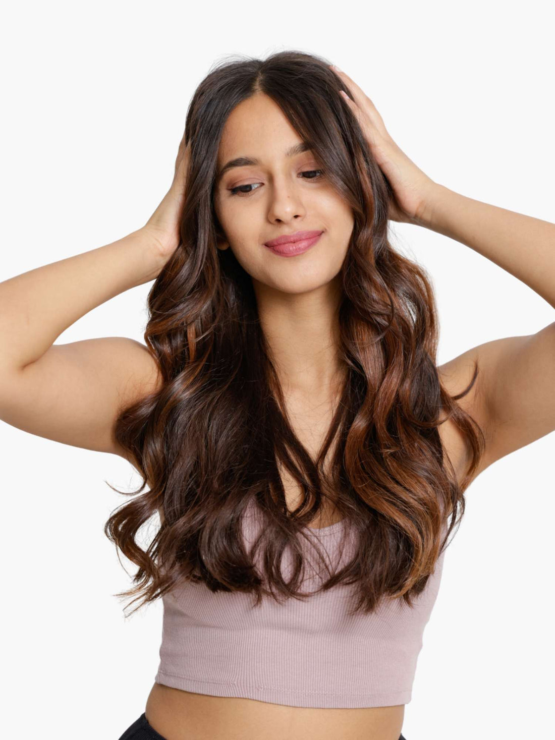 A woman with long, wavy hair with bronze streaks, posing with her hands in her hair.