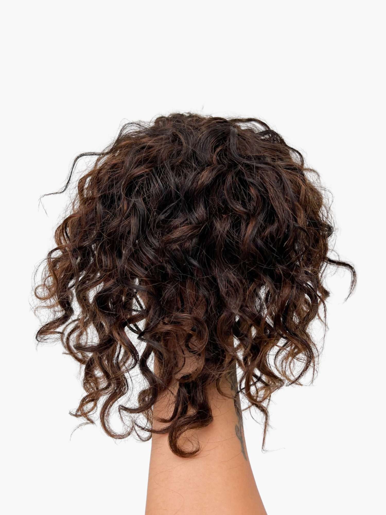 A hand holding a curly hair bun extension.